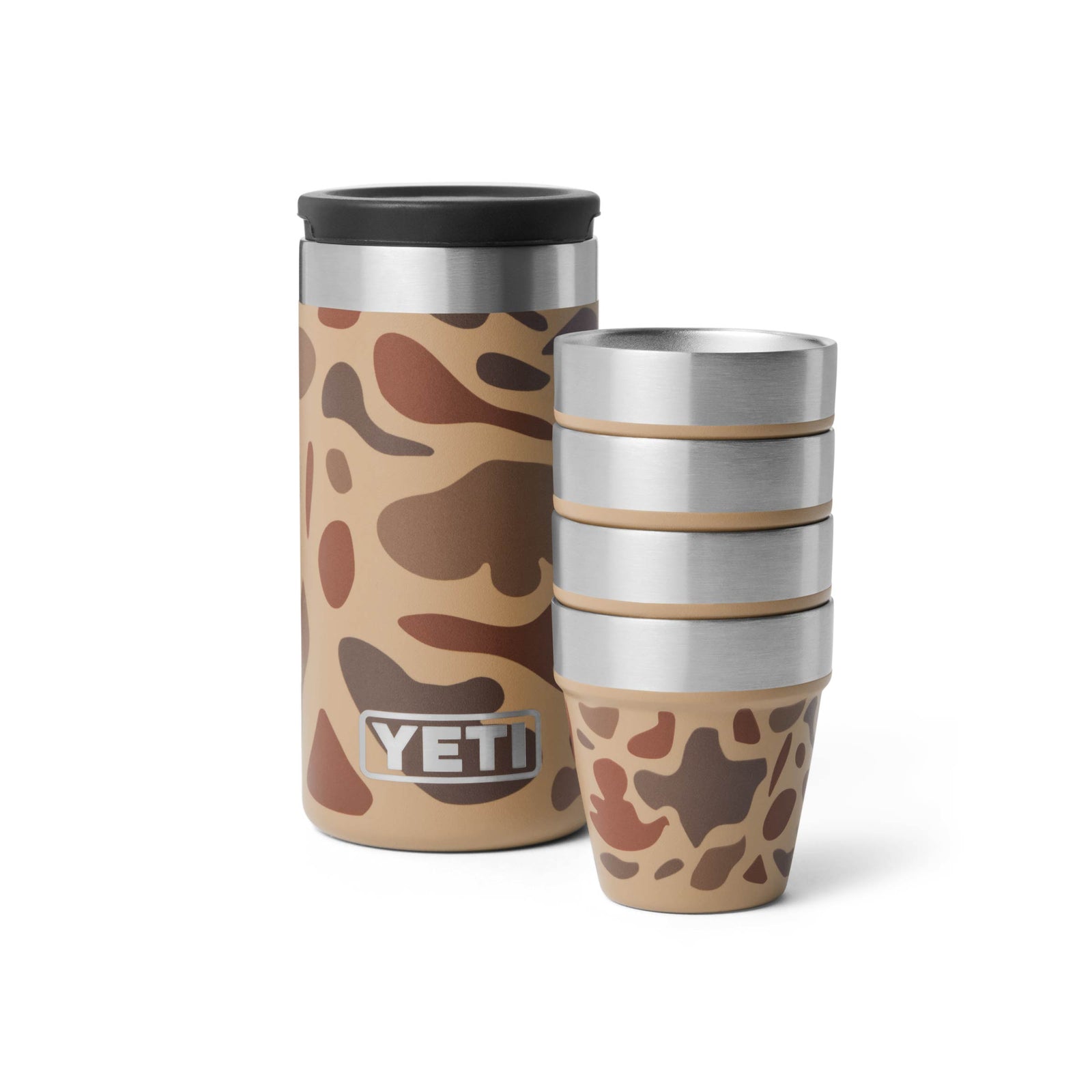 Ein YETI® Rambler Becher in Wetlands Camo steht neben einem Stapel von vier passenden YETI® Rambler Schnapsbechern, die beide das Camo-Muster und das sichtbare YETI-Branding aufweisen.