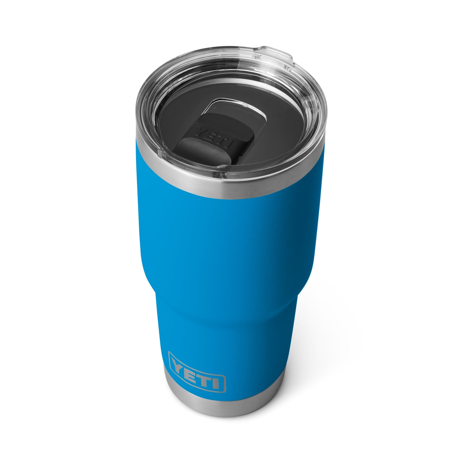 Der YETI® Reisebecher Rambler 30 Oz in Big Wave Blue ist schräg mit einem transparenten Deckel und schwarzem Schiebeverschluss auf weißem Hintergrund abgebildet. Das YETI Logo erscheint in der Nähe des Bodens dieses stylischen, auslaufsicheren Bechers.