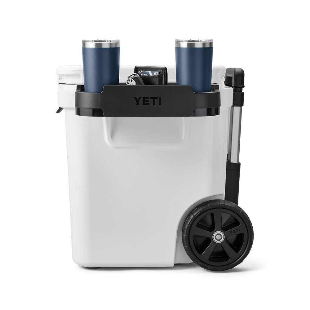 Eine weiße YETI-Kühlbox mit schwarzem Griff und Rädern verfügt über den YETI® Roadie 48/60 Dual Cupholder, der zwei blaue Reisebecher und eine Dose in seinem oberen Getränkehalter hält.