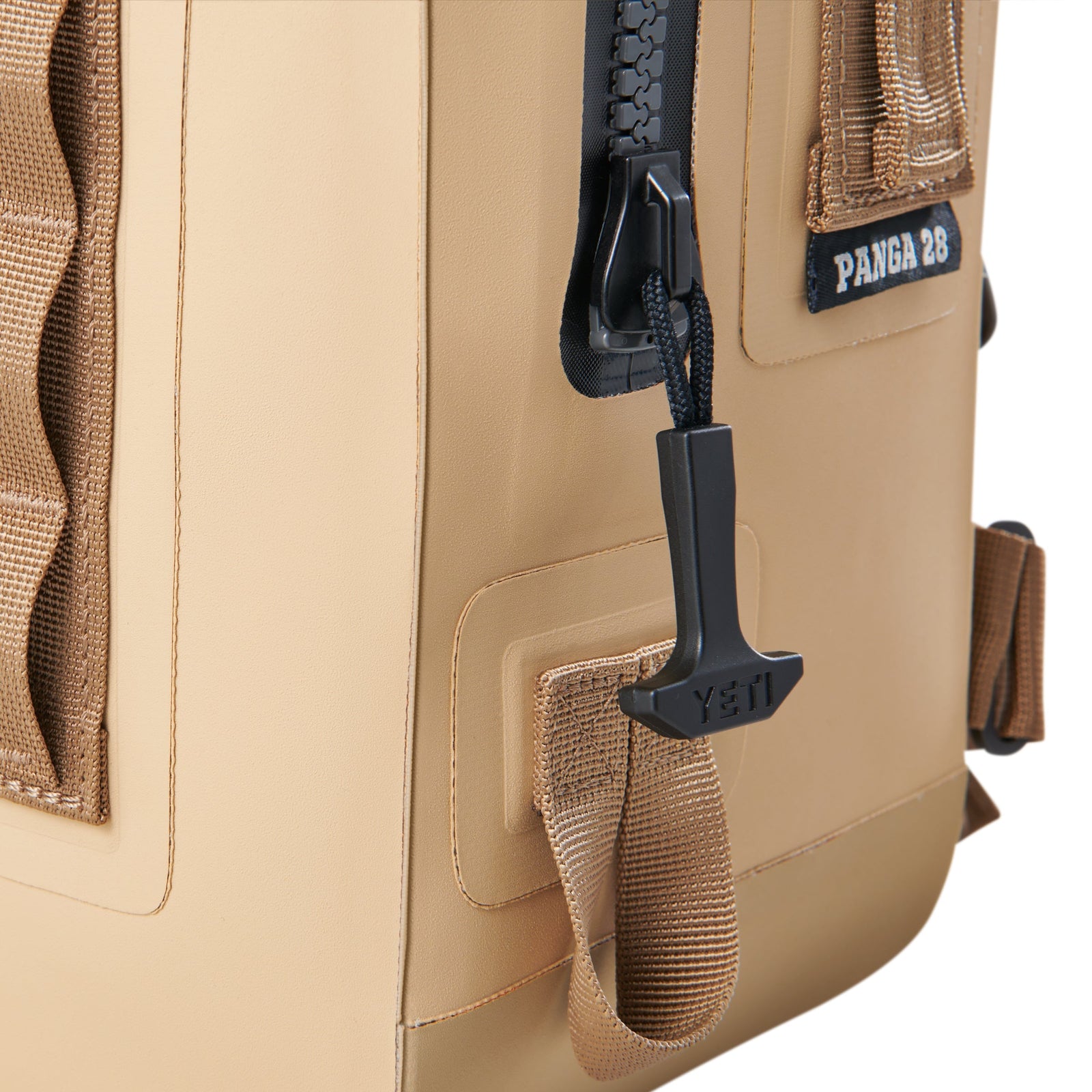 Nahaufnahme des YETI® Rucksack Panga 28 - Tan, mit schwarzem Reißverschluss mit YETI-Branding, wasserdichtem Reißverschluss und strapazierfähigen, hellbraunen Gurtbändern auf weißem Hintergrund.
