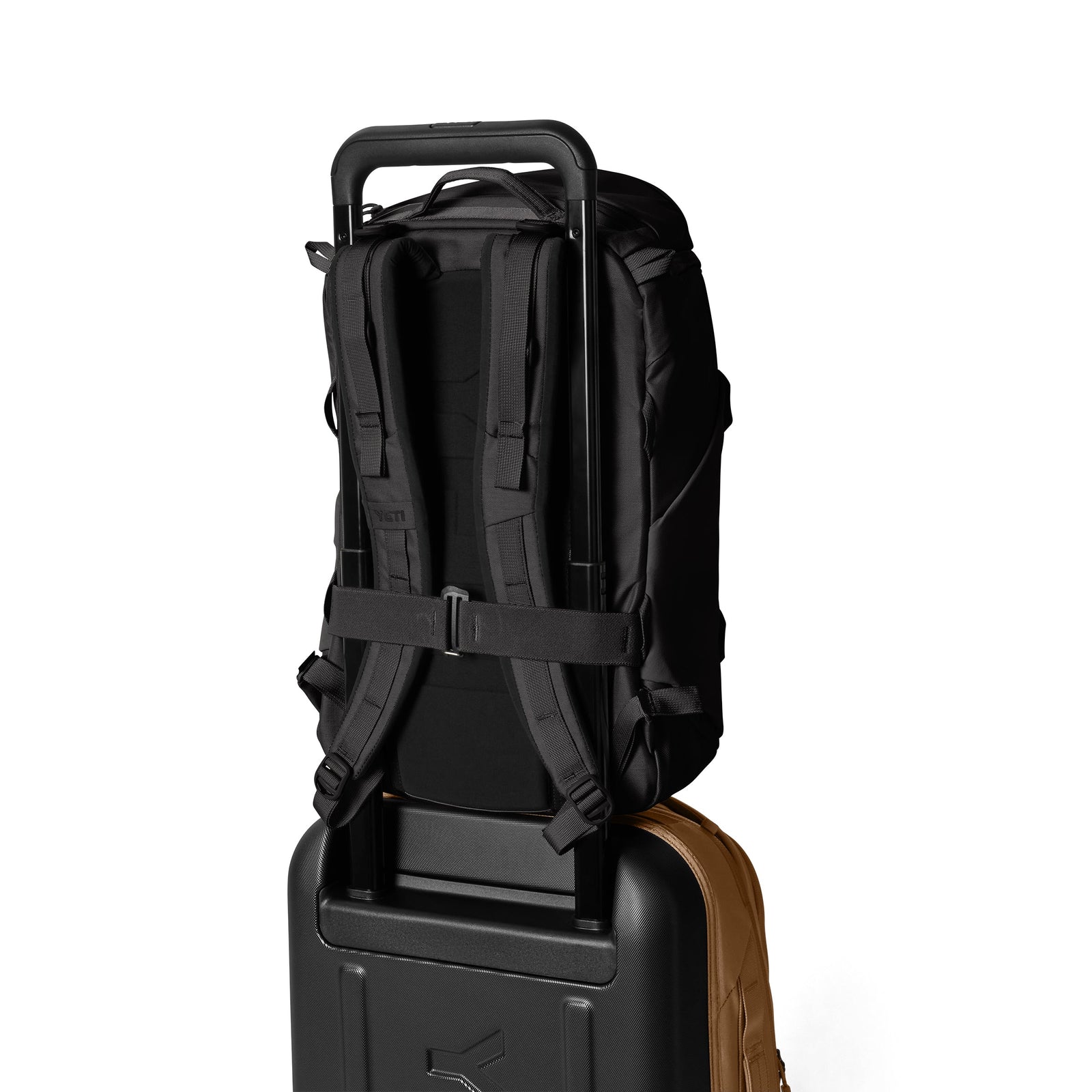 Ein YETI® Rucksack Ranchero™ 22L - Black mit gepolsterten Schulterriemen ist sicher am verlängerten Griff eines schwarzen Rollkoffers befestigt, beide stehen aufrecht vor einem schlichten weißen Hintergrund.