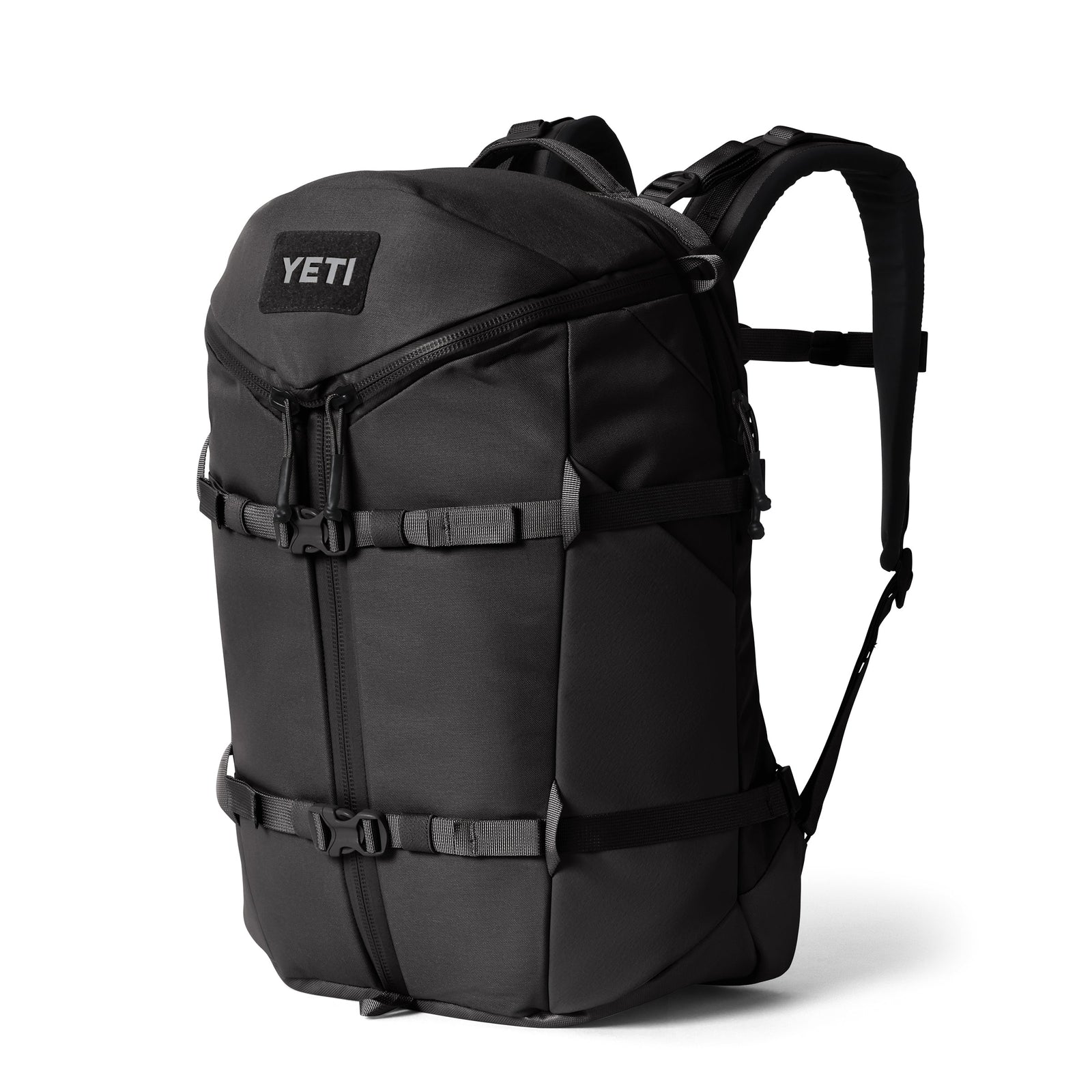 Ein YETI® Rucksack Ranchero™ 27L - Black mit gepolsterten Schultergurten, mehreren Schnallen, einer Reißverschlusstasche auf der Vorderseite und einem speziellen Laptopfach steht aufrecht vor einem schlichten weißen Hintergrund.