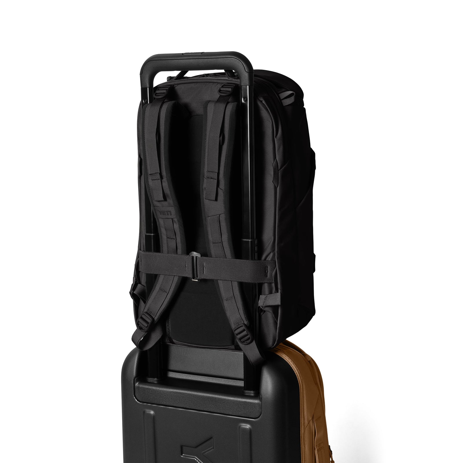 Ein YETI® Rucksack Ranchero™ 27L - Black ist sicher am Griff eines Rollkoffers befestigt, beide aufrecht vor einem schlichten weißen Hintergrund. Die wasserfeste Tasche von YETI schützt Ihre Ausrüstung, wo immer Sie reisen.
