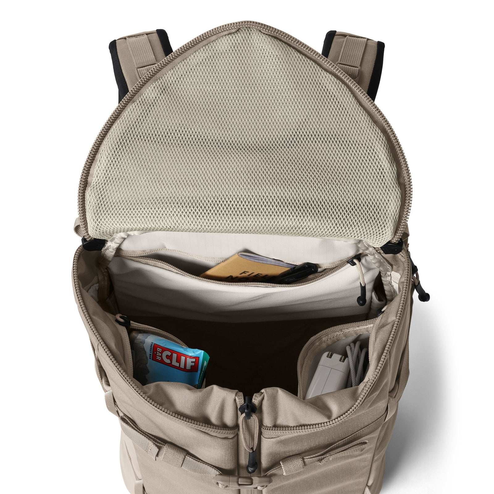 Ein offener YETI® Rucksack Ranchero™ 27L in Cape Dark Taupe bietet organisierte Fächer für einen Clif Bar, Kabel, ein Notebook und kleine Gegenstände sowie eine Netztasche im Inneren der Klappe - perfekt, um das Nötigste zu verstauen.