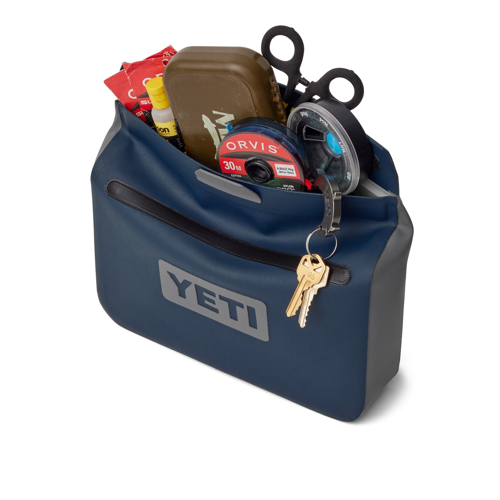 Die navyfarbene YETI® Zubehörtasche - Sidekick® 3L bietet Platz für eine Schere, Angelschnur, einen Snack-Riegel, einen Behälter und Sonnenschutzmittel. Zwei Schlüssel an einem Schlüsselring werden an den Reißverschluss der Tasche geklippt.