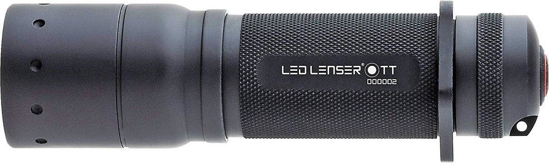 Eine schwarze, strukturierte LEDLENSER Taschenlampe TT liegt waagerecht auf weißem Hintergrund und zeigt den Markennamen und die Seriennummer - eine robuste Taschenlampe, die auf Langlebigkeit ausgelegt ist.