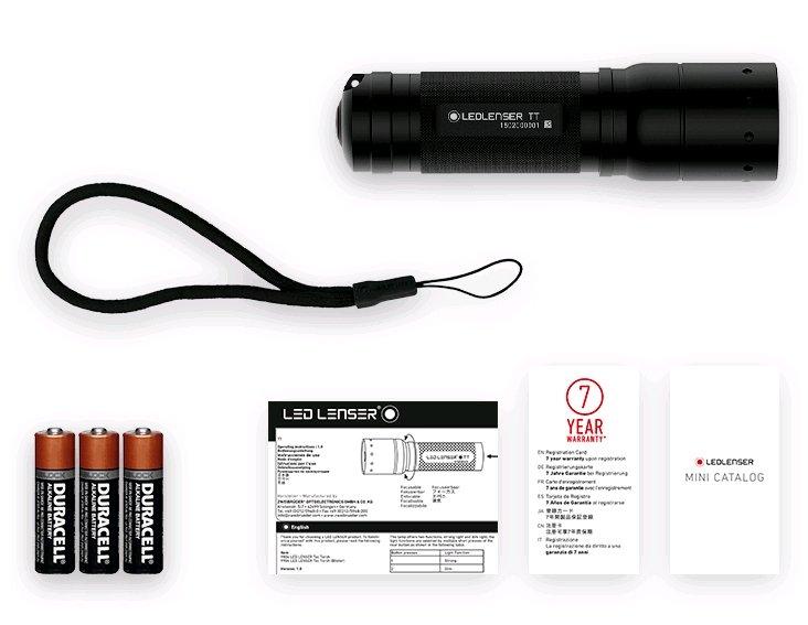 Eine schwarze LEDLENSER Ledlenser Taschenlampe TT mit Handschlaufe, drei AA Duracell-Batterien, eine Bedienungsanleitung, eine 7-Jahres-Garantiekarte und ein Mini-Katalog sind übersichtlich auf einem weißen Hintergrund angeordnet.