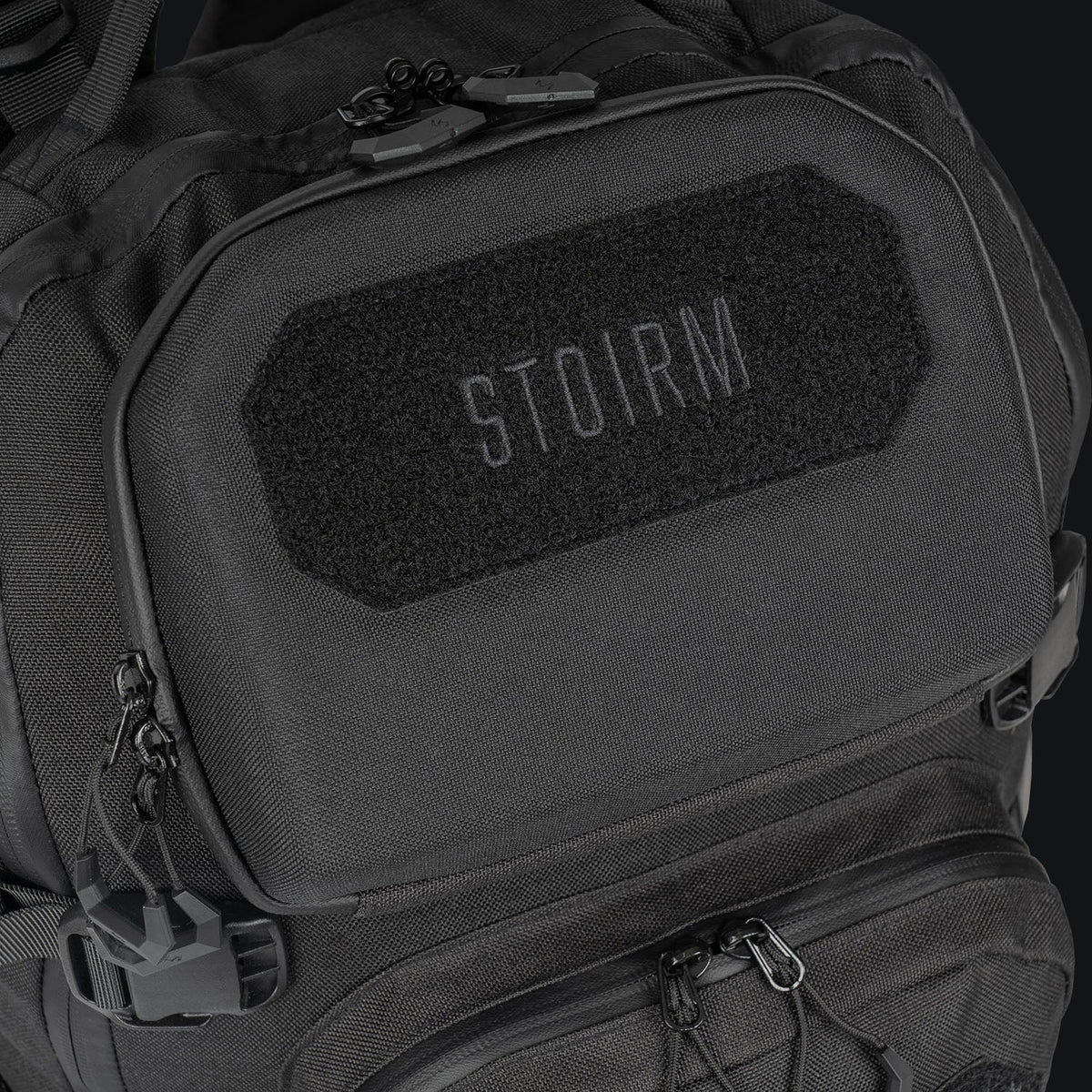 Nahaufnahme des STOIRM 25L Tactical Pack GEN2 in Ranger Green, mit einem STOIRM-Klettaufnäher auf der oberen Vordertasche, mehreren Reißverschlüssen und strapazierfähigem 1000D-Nylongewebe von STOIRM.