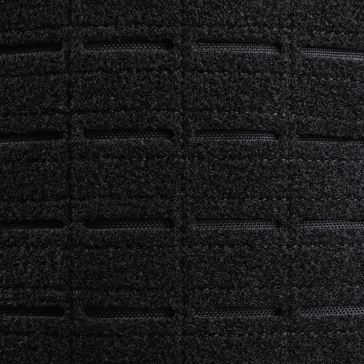 Nahaufnahme eines schwarzen, strukturierten, gitterartigen Gewebes mit genähten Linien und rechteckigen Schlitzen auf dem STOIRM 40L Tactical Pack GEN2 von STOIRM, das an robustes MOLLE-Gewebe erinnert - ideal für Outdoor-Rucksäcke oder taktische Rucksäcke.