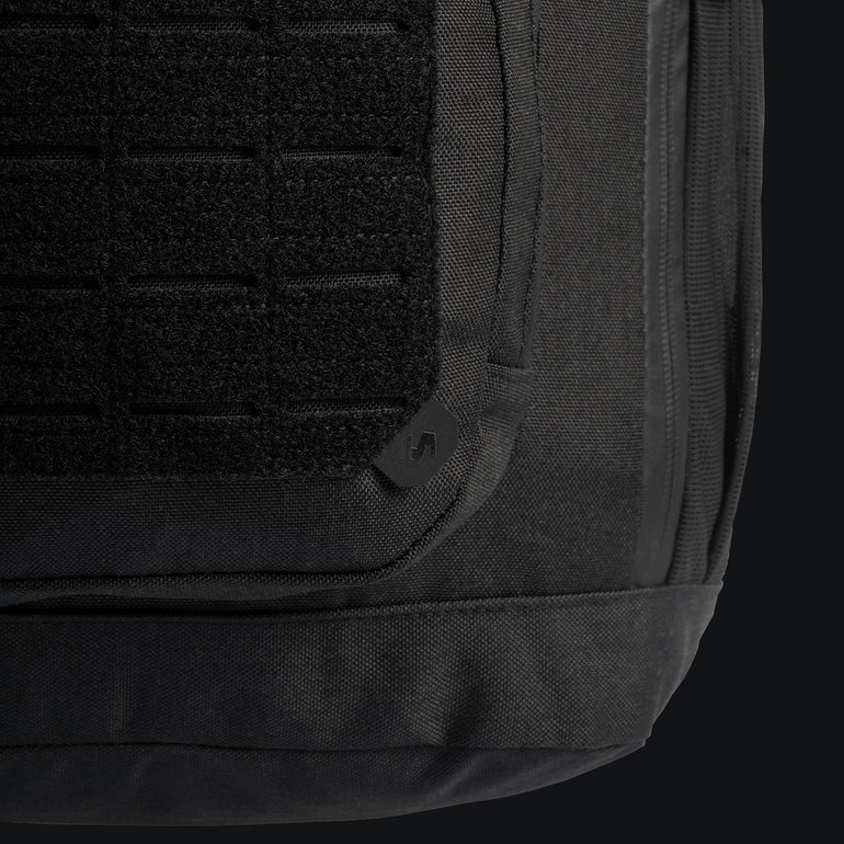 Nahaufnahme des STOIRM 40L Tactical Pack GEN2 von STOIRM, mit strukturiertem Gewebe, verstärkten Nähten und einem Aufnäher mit Gittermuster. Der dunkle Hintergrund hebt die robusten Details dieses vielseitigen Outdoor-Rucksacks hervor.