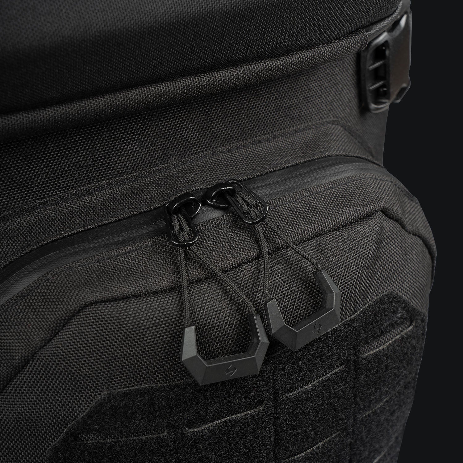 Nahaufnahme des STOIRM 25L Tactical Pack GEN2 von STOIRM in Ranger Green, die die robuste 1000D-Nylontextur und zwei geometrische Reißverschlüsse auf einer Reißverschlusstasche vor einem dunklen Hintergrund zeigt.