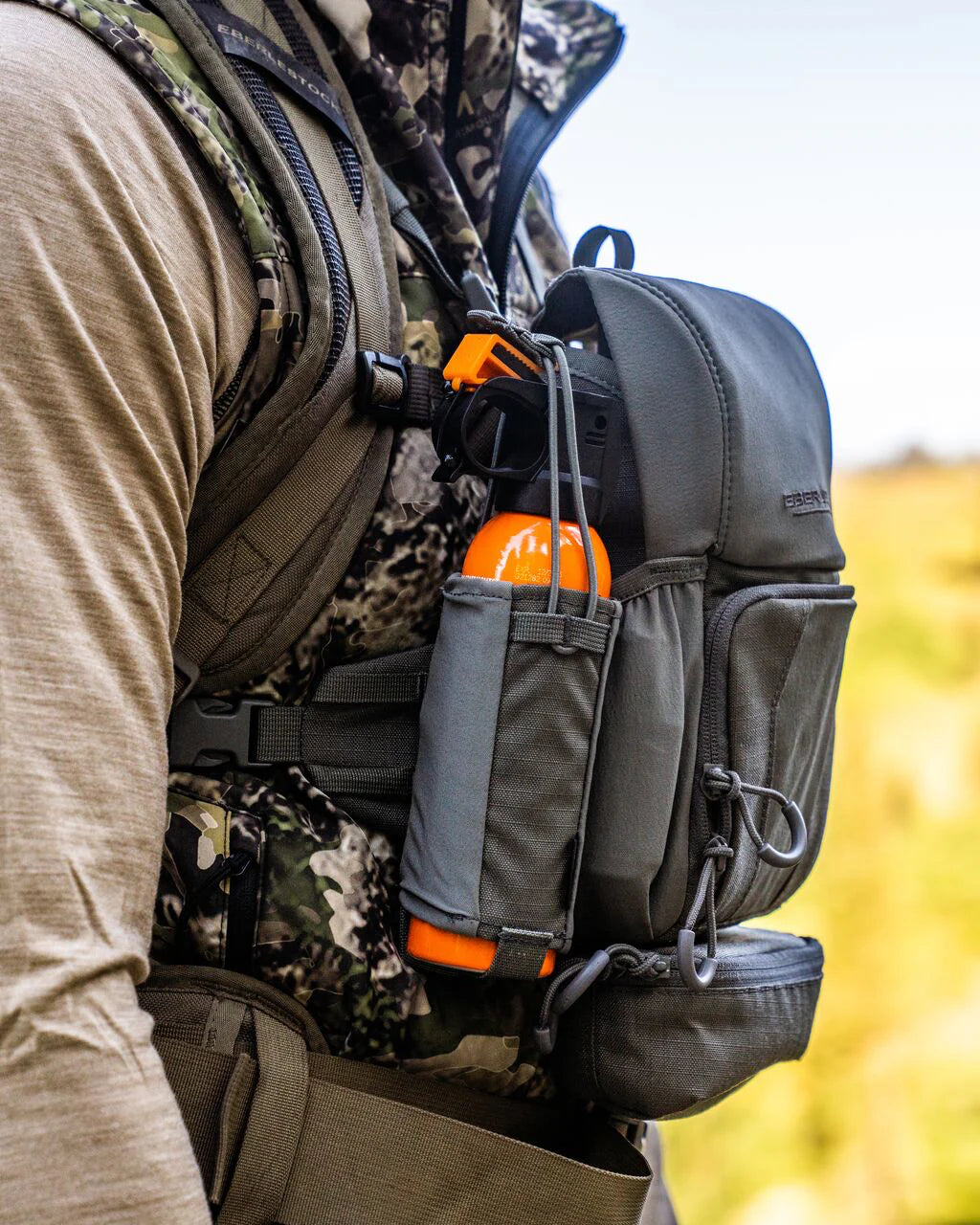 Eine Person in Tarnkleidung trägt einen grauen Brustbeutel mit einem EBERLESTOCK Recon Bear Spray Pouch und einer Ausrüstungstasche, die an einem modularen Binogurt befestigt ist.