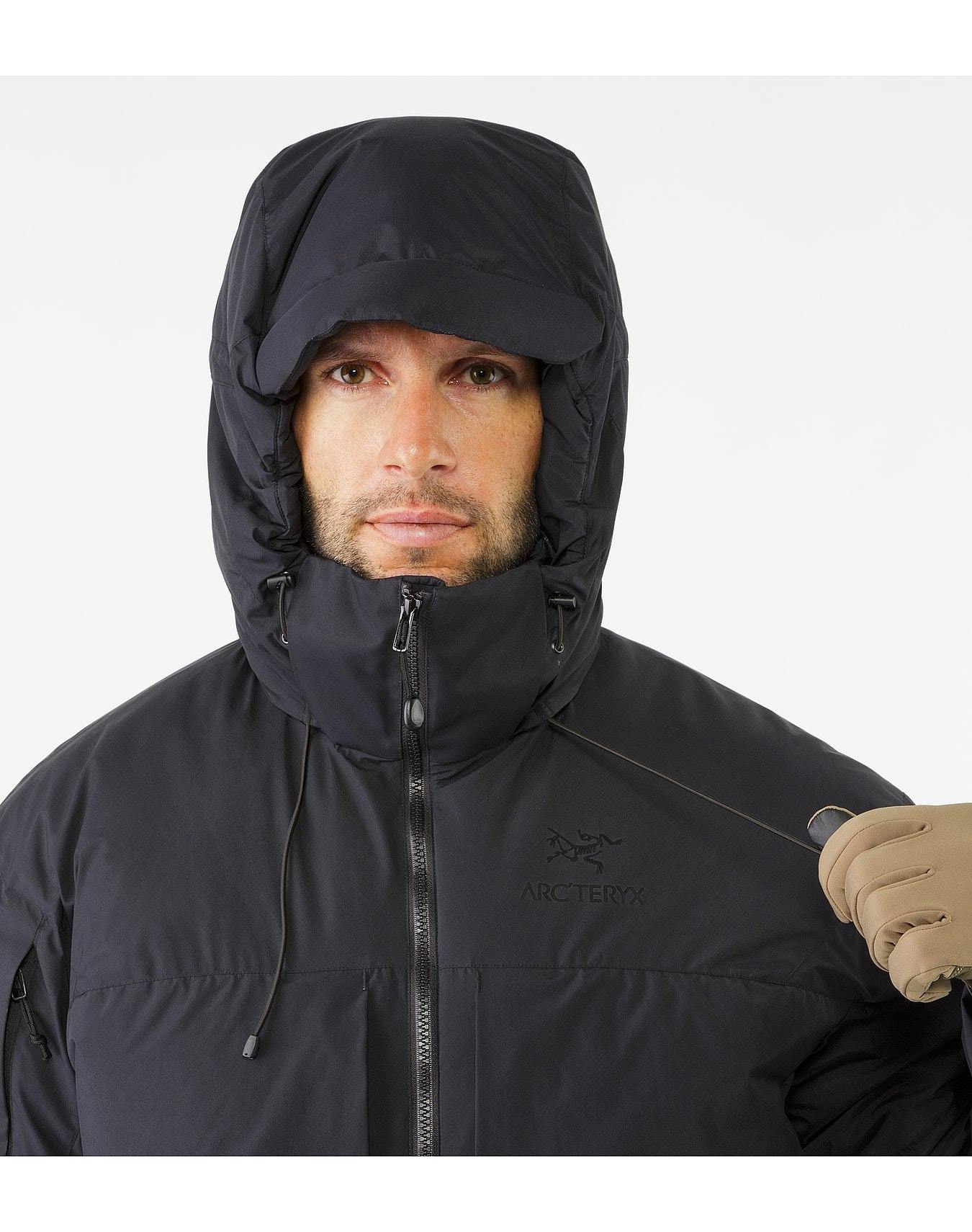 Ein Mann in einer schwarzen ARC'TERYX LEAF Cold WX Jacket SV Gen1.4 verstellt mit seinen Handschuhen die Kapuze und zieht den Kordelzug, damit sie gut sitzt. Die GORE WINDSTOPPER Jacke hebt sich von dem schlichten weißen Hintergrund ab.