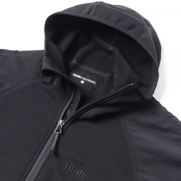 Eine Nahaufnahme eines Kojoten Tilak Femund MiG Hoody von TILAK MILITARY GEAR mit Frontreißverschluss, Markenname auf der Brust, Etikett in Größe M im Kragen, aus weichem Polartec Power Stretch Material für optimale Isolierung.