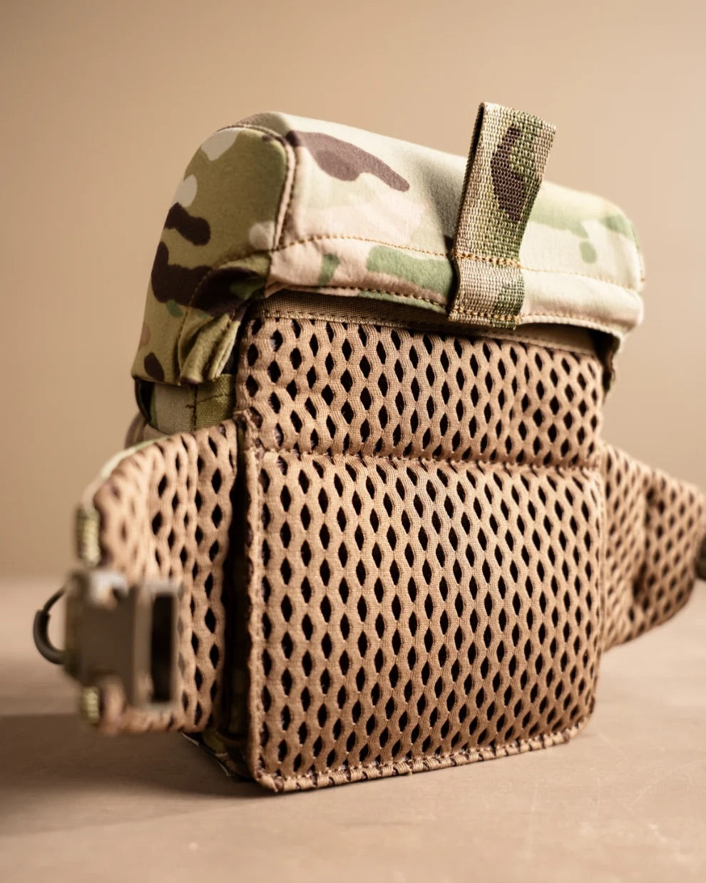 Das EBERLESTOCK Bravo Modular Bino Pack Small verfügt über eine Klappe in Tarnfarben, eine Rückwand aus braunem Netzgewebe, seitliche Riemen und eine Kunststoffschnalle, die vor einem neutralen Hintergrund abgebildet sind.