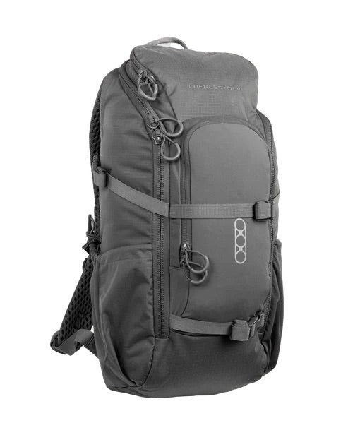 Der EBERLESTOCK Eberlestock Brute Scout, ein schwarzer, kompakter Rucksack mit mehreren Reißverschlussfächern, seitlichen Netztaschen, verstellbaren Trägern und einem Griff an der Oberseite, steht aufrecht auf einem weißen Hintergrund.