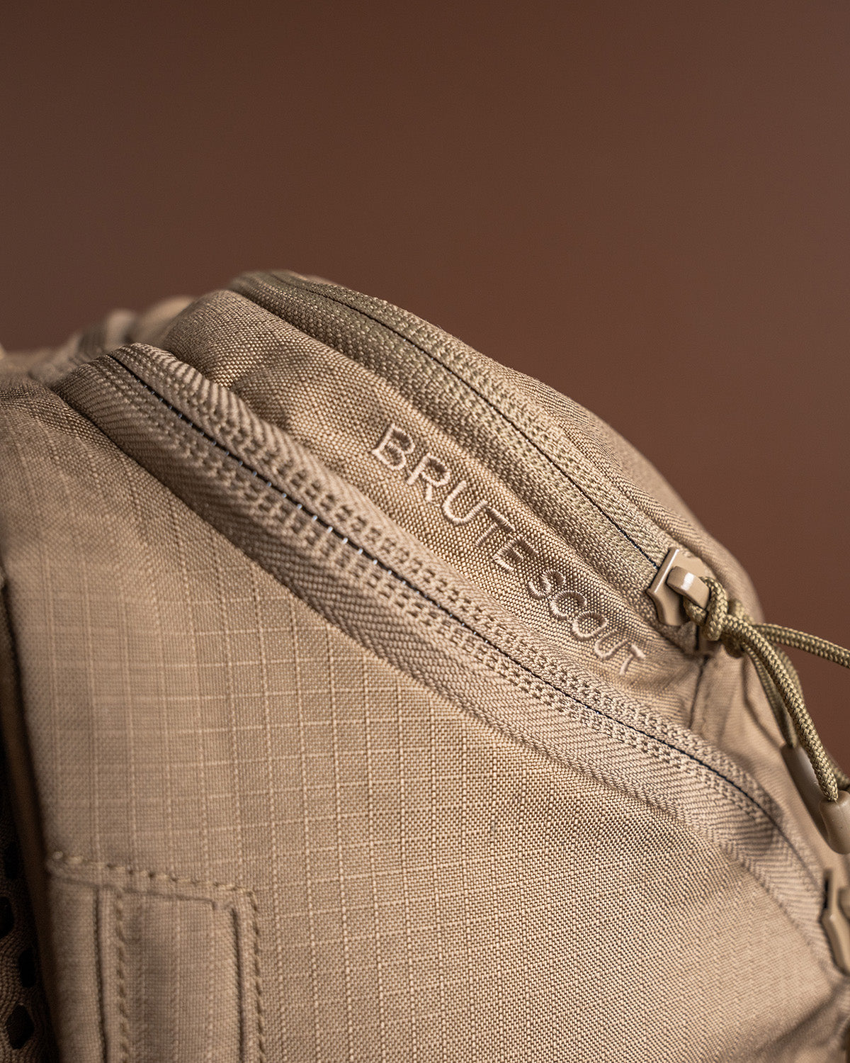 Nahaufnahme des EBERLESTOCK Brute Scout Rucksacks in Beige mit strukturiertem Stoff, Reißverschlusstasche und BRUTE-SCOUT" Stickerei - ein robuster Eberlestock Tagesrucksack für den vielseitigen Einsatz.
