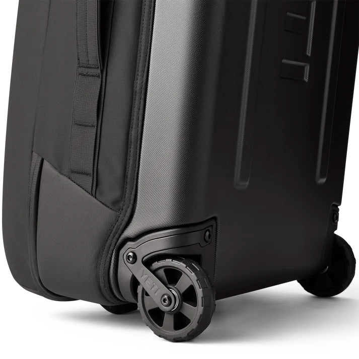 Nahaufnahme der unteren Ecke des YETI® Koffer Crossroads® 29'' - Black, mit zwei stabilen Rädern und einem Teil der robusten Hartschale mit verstärkten Seiten- und Rückwänden.