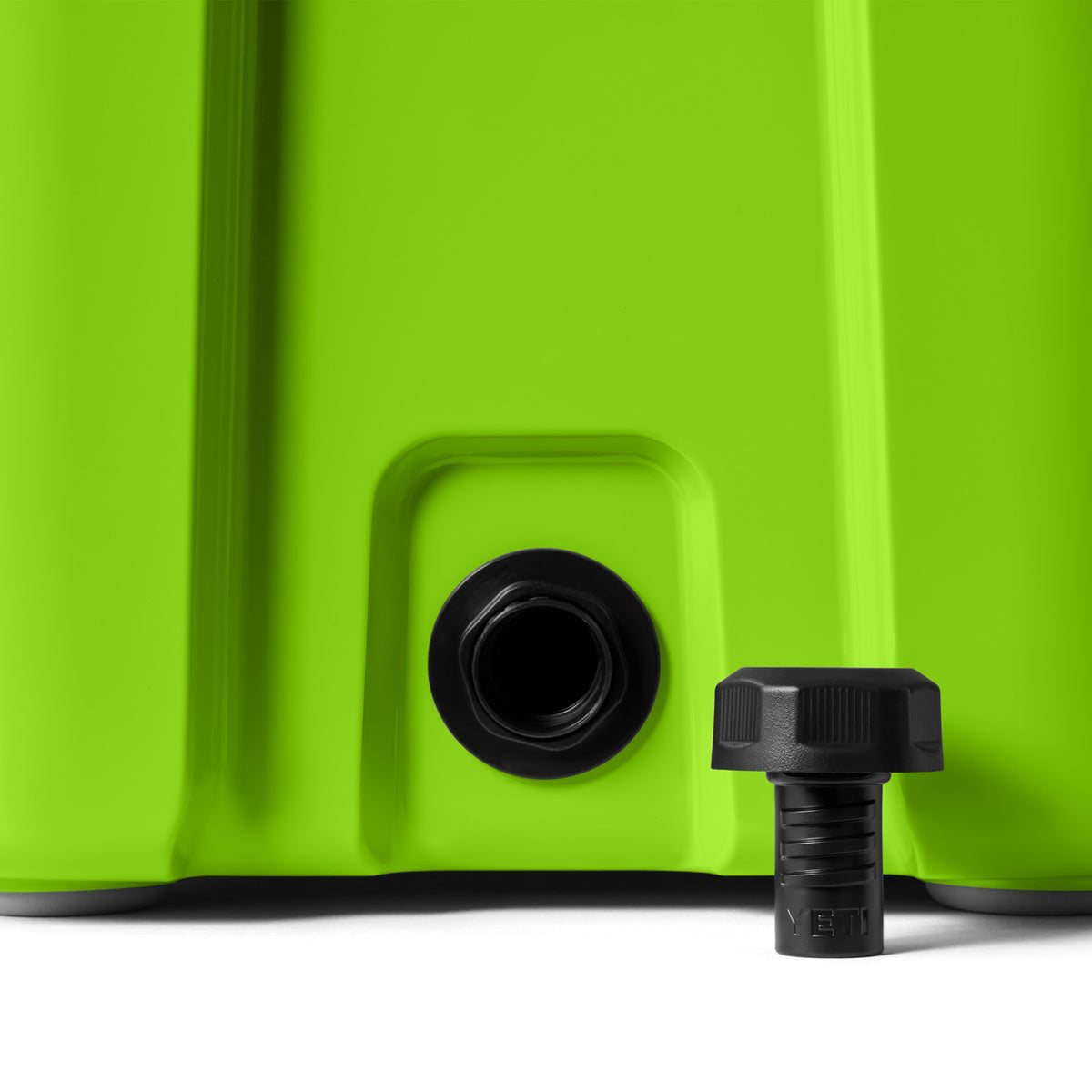 Eine Nahaufnahme einer leuchtend grünen YETI® Kühlbox Roadie 24 - Venom, bei der der schwarze Ablassstopfen entfernt und neben der Öffnung auf eine weiße Fläche gestellt wurde.