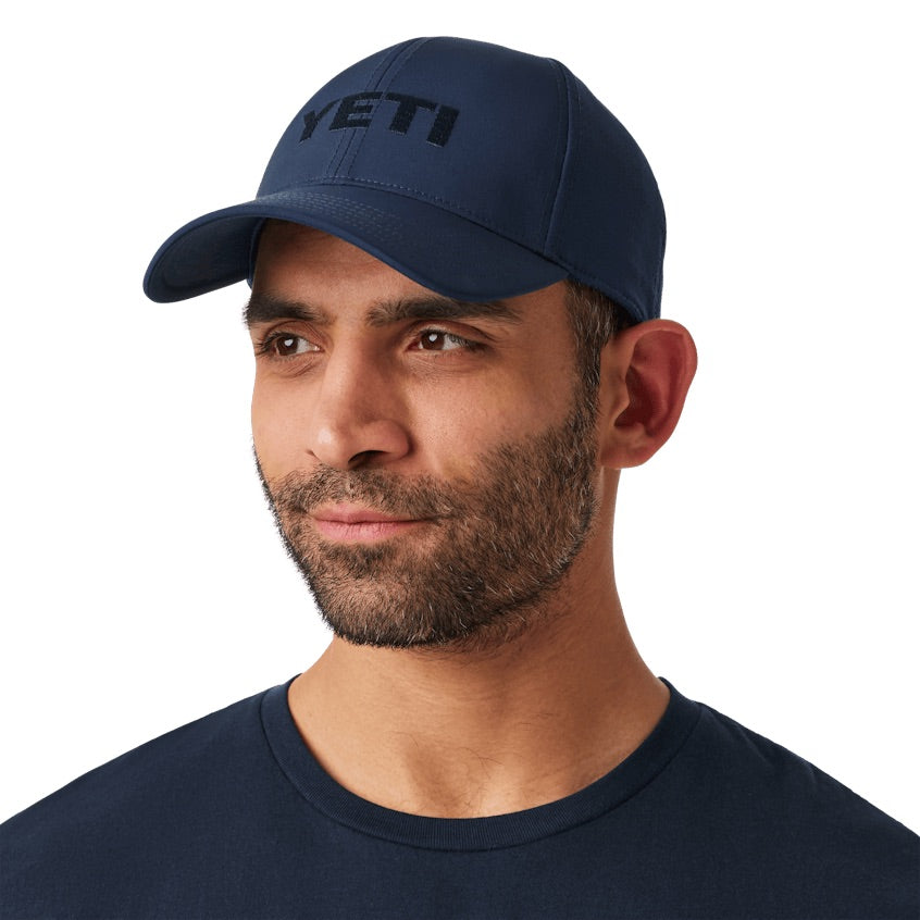 Ein Mann mit gestutztem Bart trägt eine marineblaue YETI® Structured Performance Cap und ein dazu passendes Hemd und blickt mit neutralem Blick zur Seite - der perfekte Look für Fans von YETI Outdoor-Kopfbedeckungen.