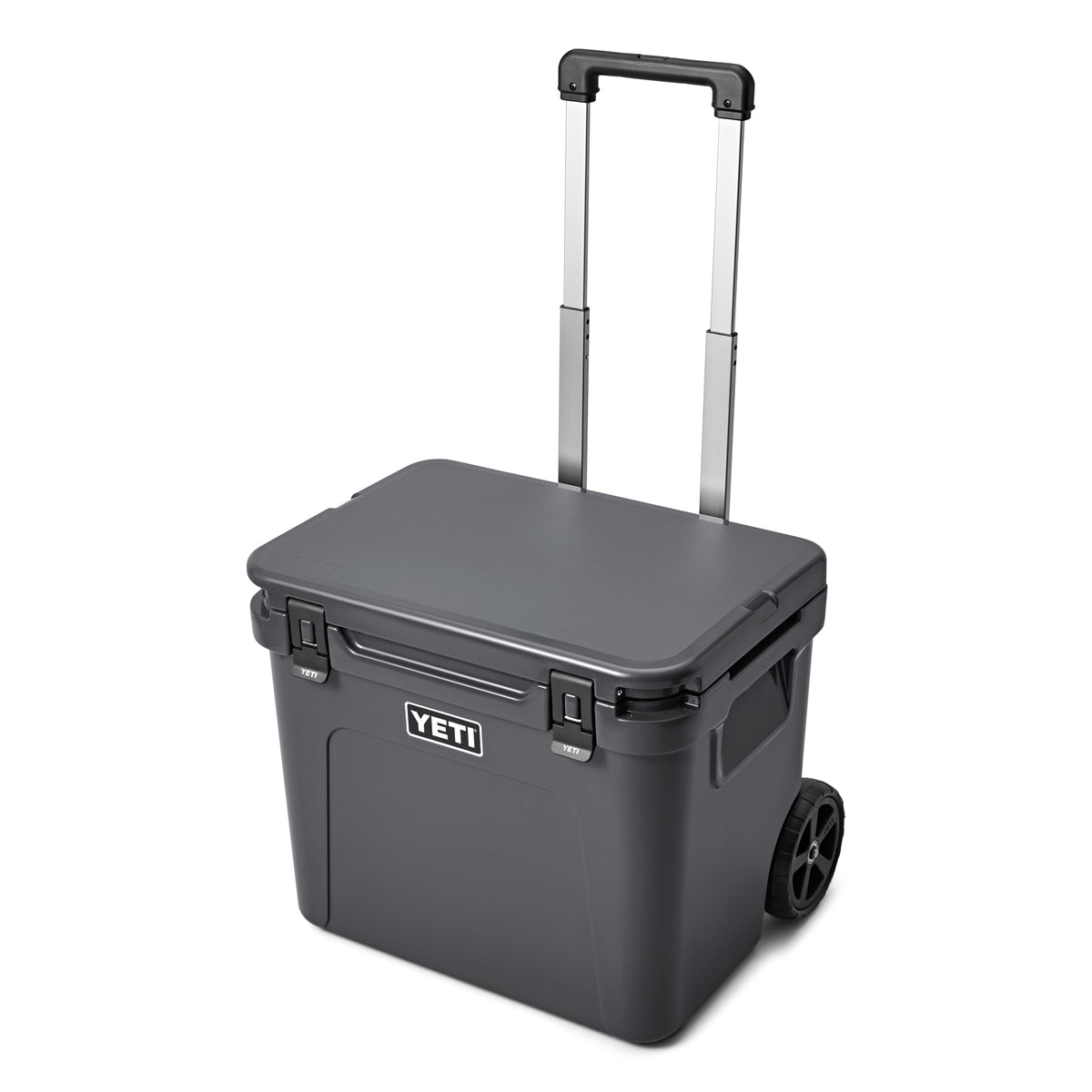 Die YETI® Kühlbox Roadie 60 - Charcoal ist eine tragbare Kühlbox mit schwarzen Rädern, einem Teleskopgriff, sicheren Frontverschlüssen und dem YETI-Logo an der Seite - ideal für den Einsatz im Freien.