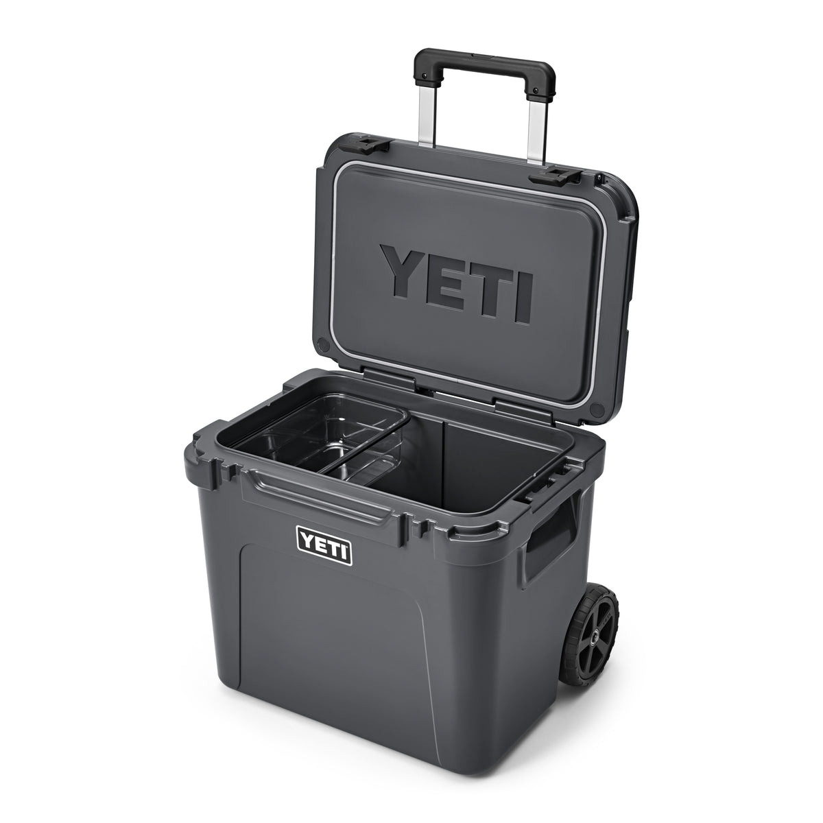 Die YETI® Kühlbox Roadie 60 in Charcoal ist geöffnet und zeigt ihren leeren Innenraum und das herausnehmbare Fach. Sie verfügt über einen Teleskopgriff, robuste Räder für den Transport und das YETI-Logo auf der Vorderseite und dem Innendeckel.