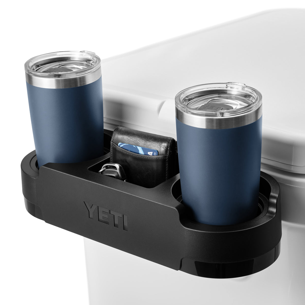 Ein schwarzer YETI Caddy auf einer weißen YETI® Kühlbox Roadie 60 fasst zwei blaue Reisebecher, eine Brieftasche und Schlüssel.
