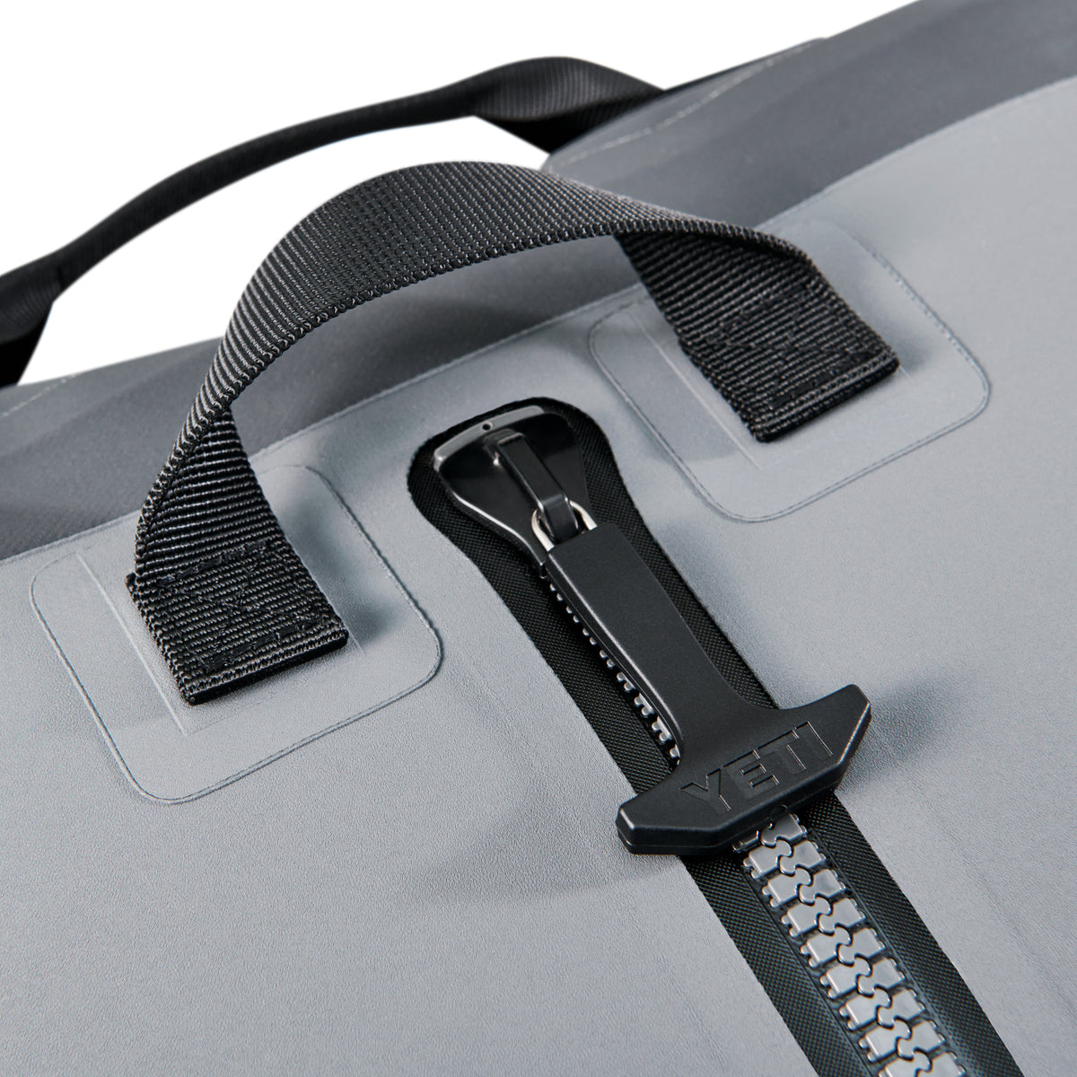Nahaufnahme der YETI® Reisetasche Panga 100 - Storm Grey, mit einem robusten Reißverschluss mit schwarzer YETI-Zuglasche und zwei verstärkten schwarzen Griffen mit sicheren Nähten.