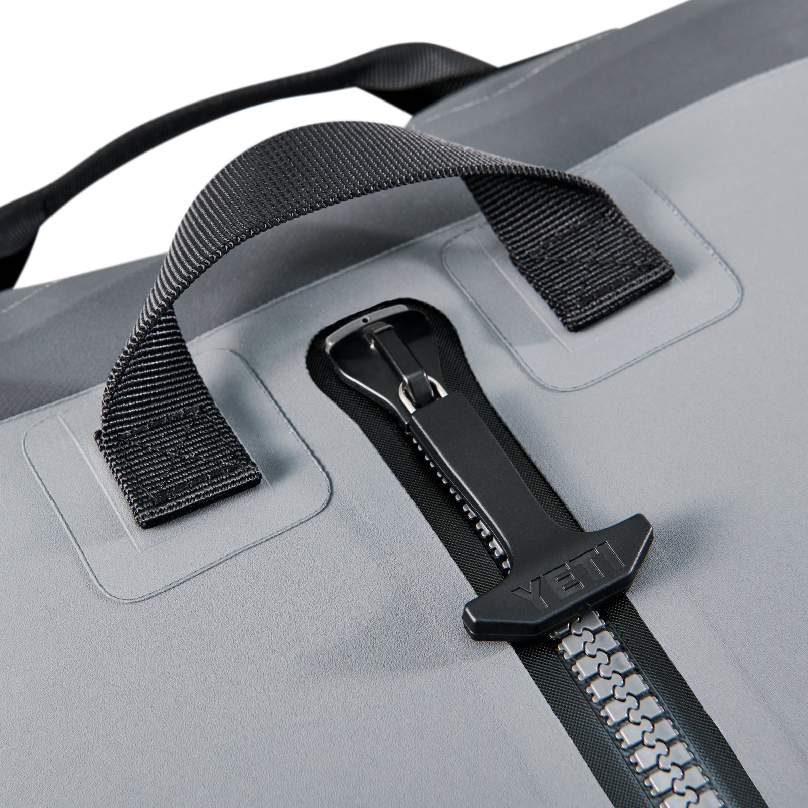 Nahaufnahme der YETI® Reisetasche Panga 100 - Storm Grey, mit einem robusten Reißverschluss mit schwarzer YETI-Zuglasche und zwei verstärkten schwarzen Griffen mit sicheren Nähten.