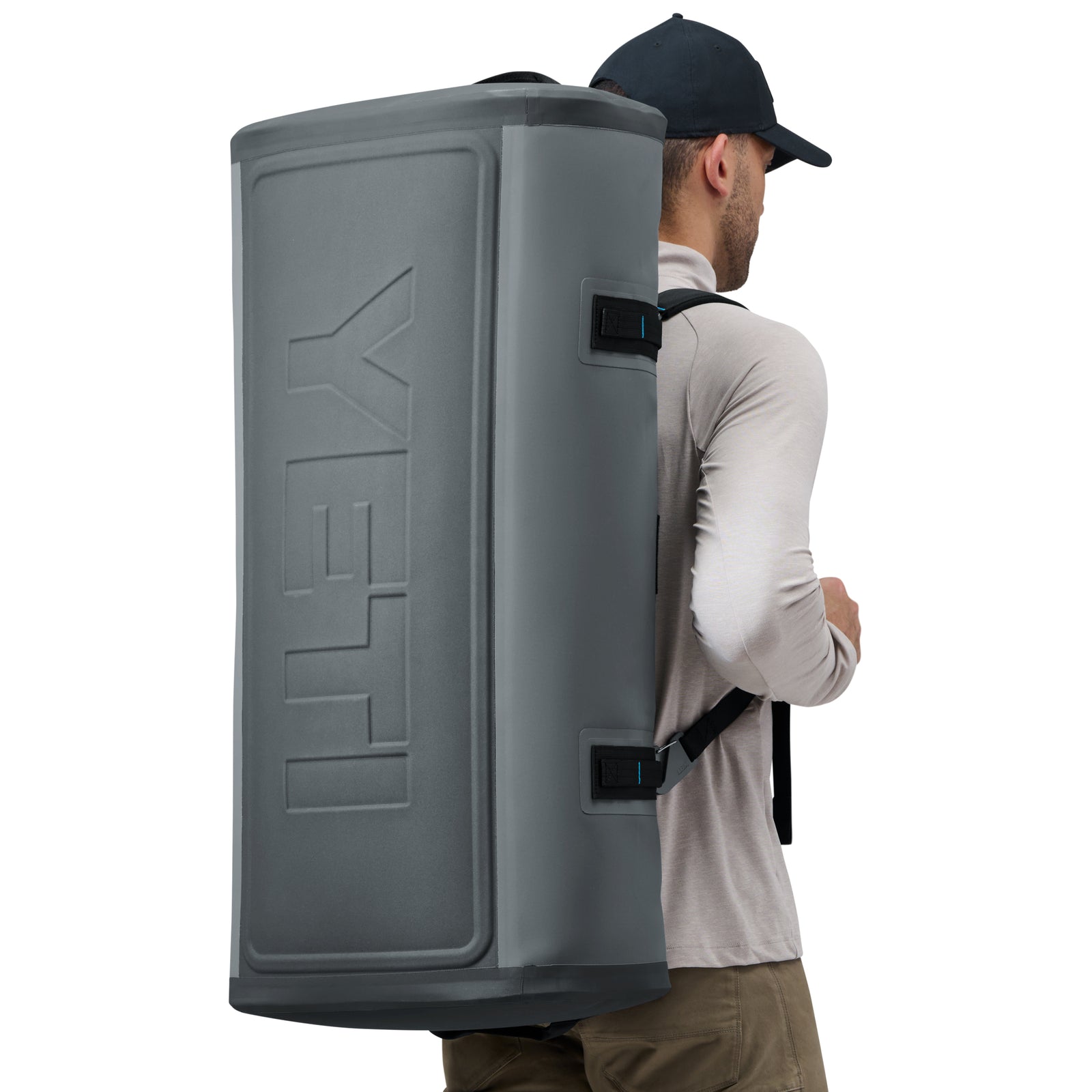 Eine Person mit dunkler Mütze und hellem Hemd trägt die YETI® Reisetasche Panga 100 - Storm Grey, einen großen wasserdichten Seesack mit geformten Seiten und auffälligem YETI-Branding, auf dem Rücken. Man sieht sie von der Seite.