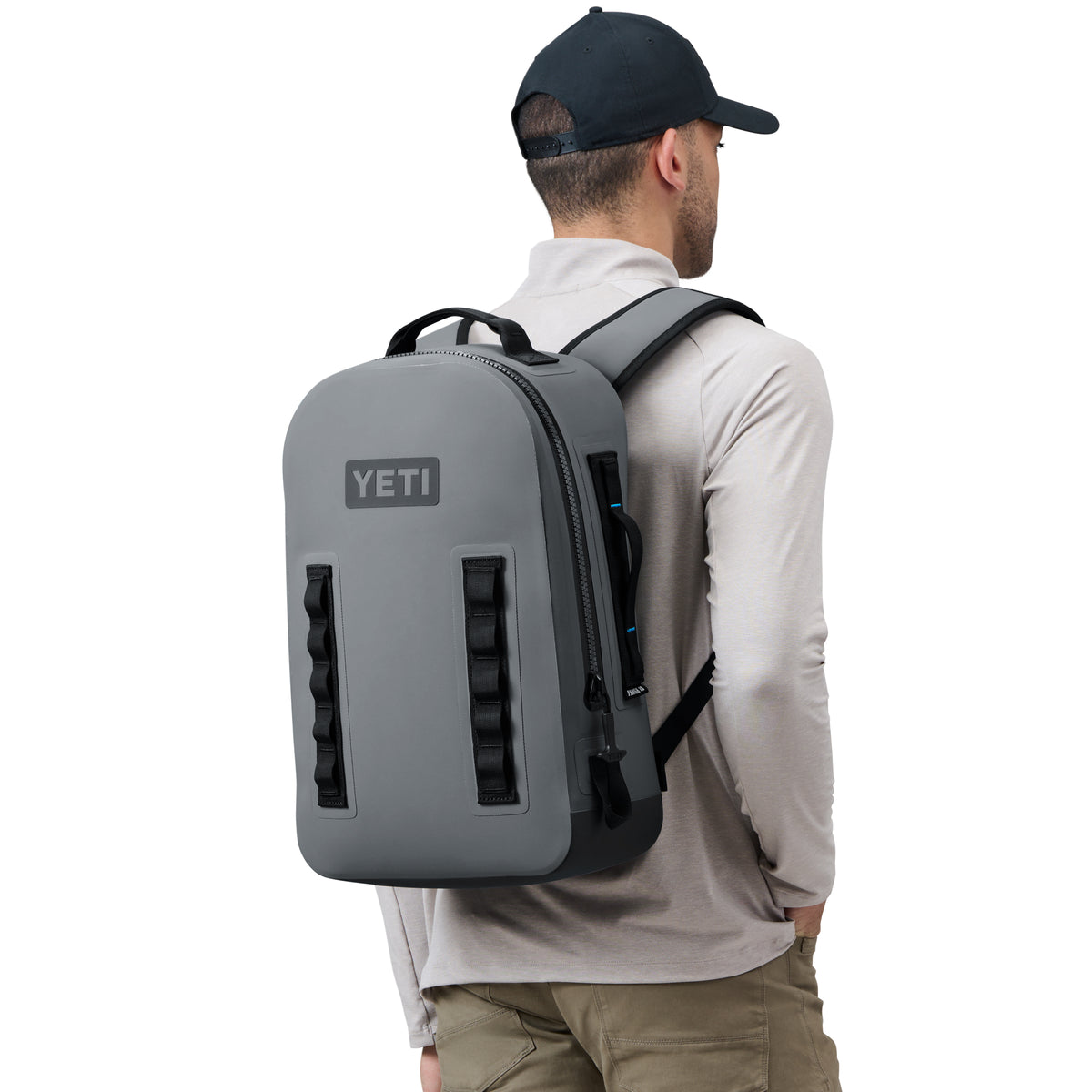 Eine Person, die eine schwarze Mütze und ein hellgraues langärmeliges Hemd trägt, ist von hinten zu sehen. Sie trägt einen YETI® Rucksack Panga 28 in Storm Grey mit schwarzen Gurten und Details.
