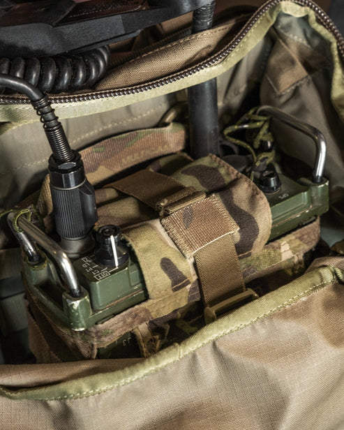 Eine Nahaufnahme eines militärischen Funkgeräts im Inneren des EBERLESTOCK FAC Track - Military Green, mit seinen Bedienelementen, Metallgriffen und dem Spiralkabel - ideal für taktische Einsätze.