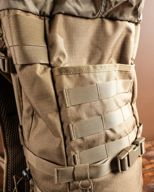 Nahaufnahme des EBERLESTOCK Gunrunner Pack - Loden. Hervorzuheben sind die robuste Nylonkonstruktion, das MOLLE-Gurtband für Befestigungen, die seitlich verstellbaren Riemen mit Schnallen und das integrierte Scheidenfach für die sichere Aufbewahrung von Waffen.
