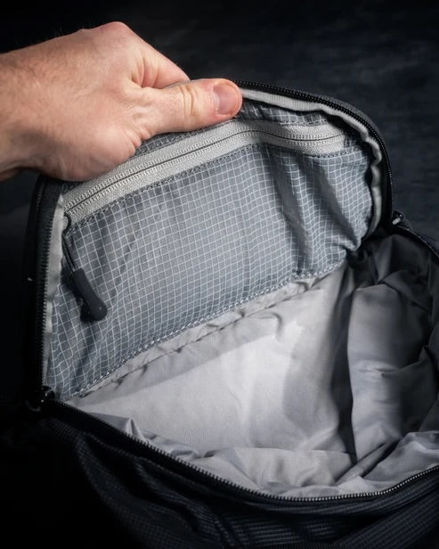 Eine Hand öffnet den Deckel der EBERLESTOCK Fade Sling XL und zeigt die Innentasche mit Reißverschluss und das geräumige Hauptfach vor einem dunklen Hintergrund.