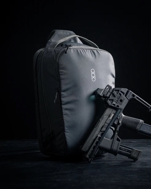 Ein taktischer Rucksack von EBERLESTOCK steht aufrecht auf einer dunklen Oberfläche, mit dem Eberlestock Fade Sling XL in der Nähe - beides hebt sich vom Hintergrund ab und ist ideal, um Ihre EDC-Ausrüstung zu organisieren.