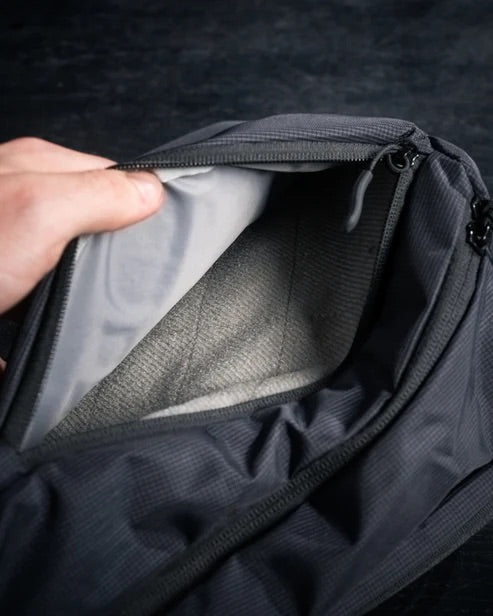 Eine Hand öffnet das Hauptfach der EBERLESTOCK Fade Sling XL, einer dunkelgrauen Umhängetasche, und zeigt das hellgraue Innere, das sich perfekt für die Organisation Ihrer wichtigsten Dinge eignet, vor einem dunklen Hintergrund.