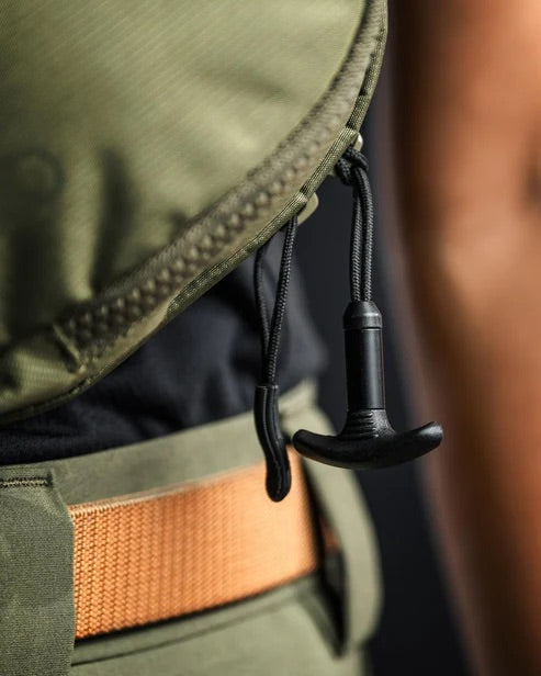 Eine Person trägt olivgrüne Outdoor-Kleidung und einen orangefarbenen Gürtel, der die EBERLESTOCK Fade Flex Micro mit schwarzem Kordelzug und Kunststoffknebel an der Reißverschlusstasche zeigt - perfekt für den Transport Ihrer EDC-Utensilien.