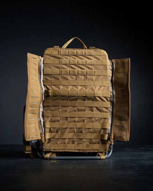 Ein hellbrauner EBERLESTOCK-Rucksack mit MOLLE-Gurtband steht aufrecht vor einem dunklen Hintergrund, beide Seitenwände lassen sich mit der Eberlestock EMOD Reissverschluss Erweiterung öffnen und geben den Blick auf das Innere frei.