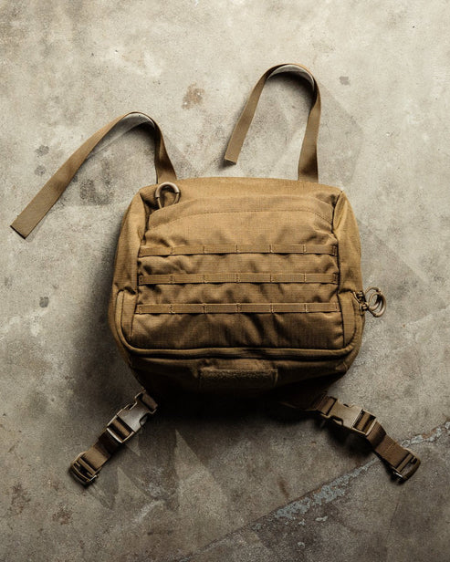 Der EBERLESTOCK Mission Lid, ein hellbrauner taktischer Rucksackdeckel mit Gurtband an der Vorderseite, zwei Schultergurten und zwei Bodengurten mit Schnallen für zusätzlichen Stauraum (Mission System kompatibel), ruht auf einer strukturierten Betonoberfläche.