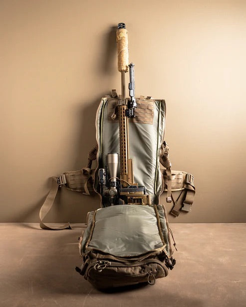 Ein geöffneter brauner EBERLESTOCK Eberlestock Spectre taktischer Rucksack offenbart ein zerlegtes Scharfschützengewehr und ein Zielfernrohr vor einem beigen Hintergrund - ideal für die Jagd oder Outdoor-Missionen. Der Lauf des Gewehrs ragt aus der Tasche heraus.