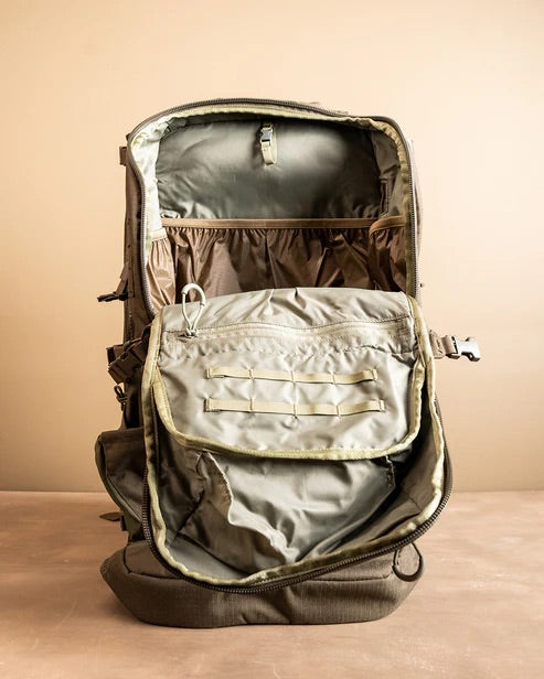 Ein khakifarbener EBERLESTOCK Spectre-Rucksack wird vor einem beigen Hintergrund mit geöffnetem Reißverschluss gezeigt, der seine zahlreichen Innenfächer und Taschen zeigt.