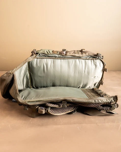 Ein offener, leerer EBERLESTOCK Spectre Rucksack liegt auf dem Rücken, der Reißverschluss ist geöffnet und gibt den Blick auf geräumige Fächer und Netztaschen vor einem schlichten, beigen Hintergrund frei.