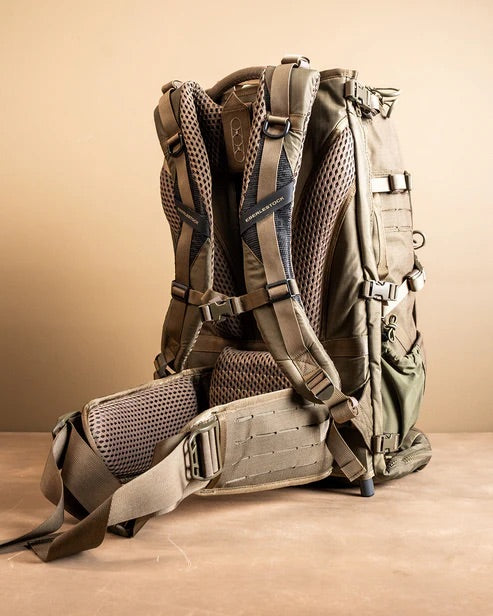 Der ultraleichte EBERLESTOCK Spectre Jagdrucksack in khaki und olivgrün steht aufrecht auf einer hellbraunen Fläche und zeigt seine gepolsterten Schultergurte, das Netzrückenteil, den verstellbaren Hüftgurt und die zahlreichen Schnallen.