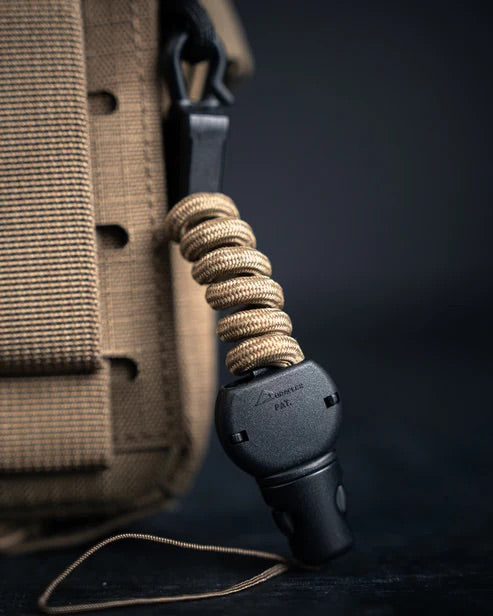 Nahaufnahme einer hellbraunen EBERLESTOCK Mag-Free Rangefinder Pouch mit einer Paracord-Schnur, die an einer schwarzen Sicherheitspfeife befestigt ist, vor einem dunklen Hintergrund.