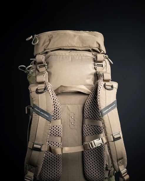 Ein khakifarbener EBERLESTOCK Brute 4500 Rucksack mit gepolsterten Schultergurten, Netzeinsätzen und mehreren Fächern ist vor einem dunklen Hintergrund abgebildet, wobei der EBERLESTOCK Markenname auf den Gurten sichtbar ist.