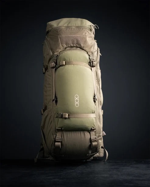 Ein olivgrüner EBERLESTOCK Brute 4500 Wanderrucksack mit mehreren Fächern und Gurten steht aufrecht vor einem dunklen Hintergrund. Auf der Vordertasche des modularen Rucksacks befindet sich ein weißes geometrisches Logo.