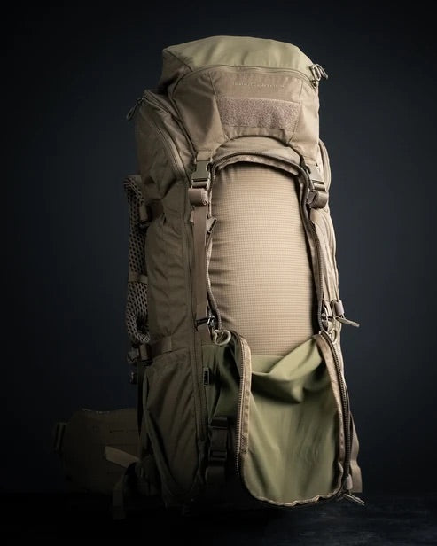 Der EBERLESTOCK Brute 4500, ein großer khakifarbener Militärrucksack mit mehreren Fächern, offener Fronttasche und sichtbaren seitlichen Netztaschen, steht aufrecht auf einer dunklen Oberfläche.