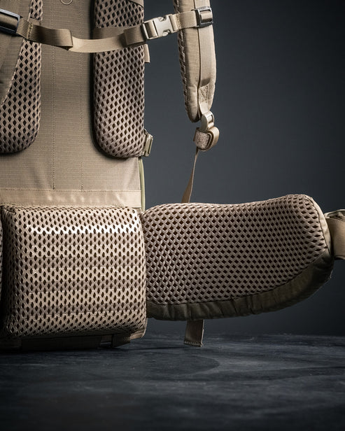 Nahaufnahme des EBERLESTOCK Brute 4500, eines braunen modularen Rucksacks mit gepolsterten, atmungsaktiven Mesh-Schultergurten und Hüftgurt für ergonomischen Komfort, vor dunklem Hintergrund.