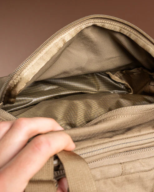 Eine Hand öffnet den Reißverschluss eines EBERLESTOCK Brute 3500 Rucksacks und gibt den Blick auf das leere, beigefarbene, gestreifte Innere frei - perfekt für jedes Outdoor-Abenteuer.