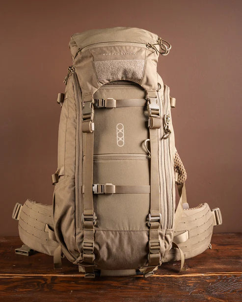 Der EBERLESTOCK Brute 3500 ist ein großer brauner, modularer Rucksack mit mehreren Riemen, Schnallen, einem Deckelfach und Seitentaschen - perfekt für Outdoor-Touren. Er steht aufrecht auf einer hölzernen Oberfläche vor einem braunen Hintergrund.